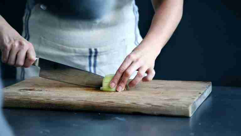 person slicing green vegetable on a cutting board